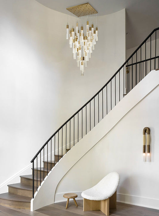 The ADS06C41G 41-light gold chandelier suspended in a bright, modern foyer featuring a curved white staircase with black railings, a minimalist white chair, and light wood accents.