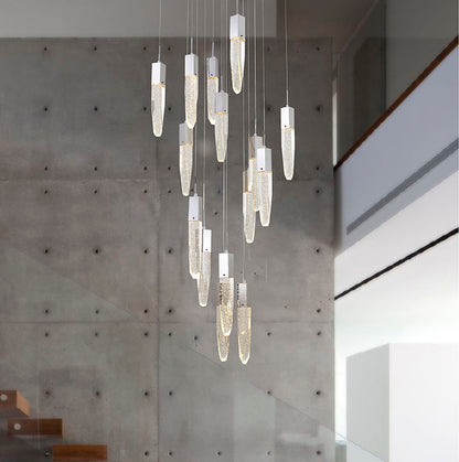 A 24-light cascading chandelier with chrome-capped, cylindrical seeded crystal pendants suspended at varying heights against a modern concrete wall in a high-ceiling foyer.