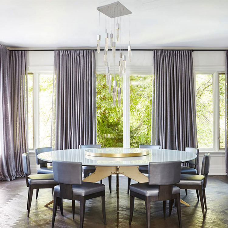 The ADS22C24CH crystal pendant chandelier centered over a large round dining table in a brightly lit room with floor-to-ceiling grey curtains.