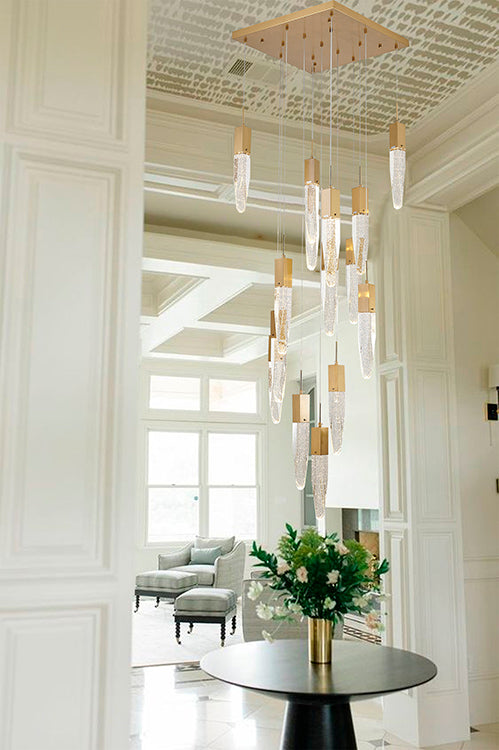 The ADS22C24G 24-light chandelier with gold-capped seeded crystal pendants cascading over a round black entry table in a bright, white-paneled grand foyer.