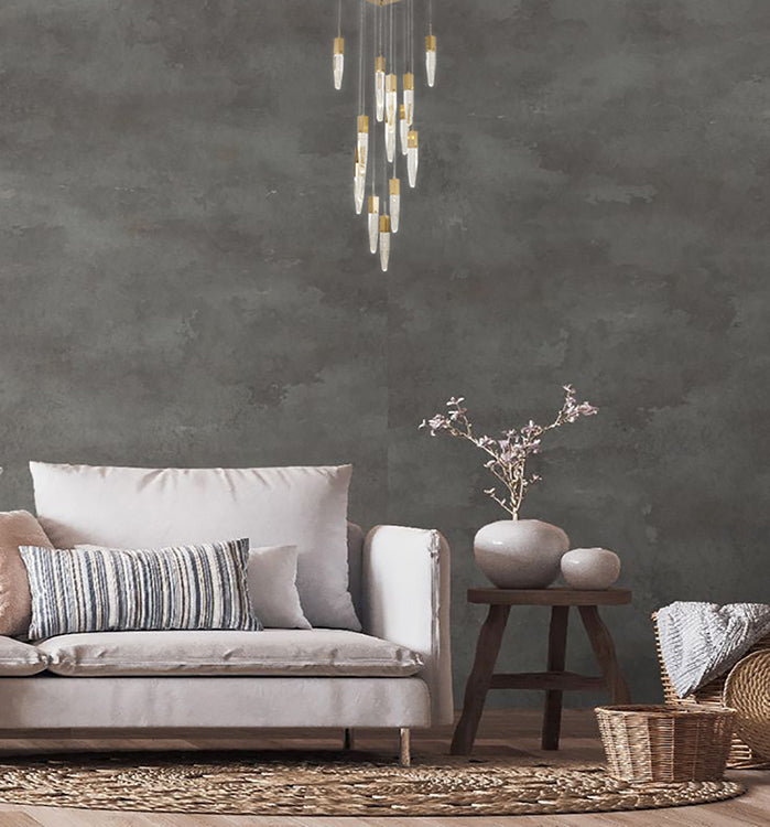 A wide shot of the gold crystal chandelier hanging in a contemporary living room with a neutral sofa and dark accent wall.